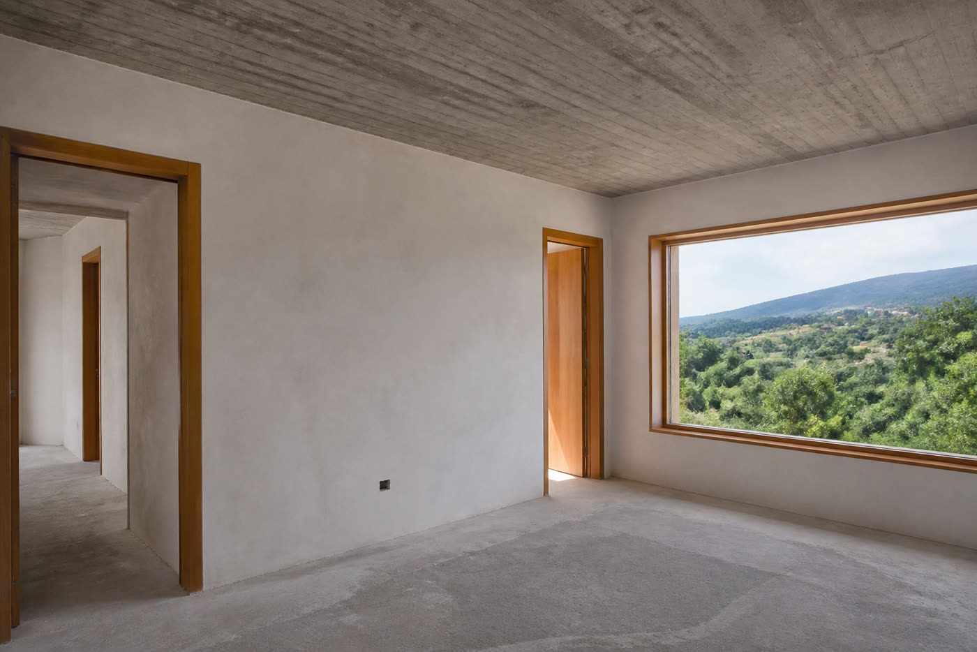 Interior de moradia: tecto de betão à vista, caixilharia de madeira e vista para o exterior.